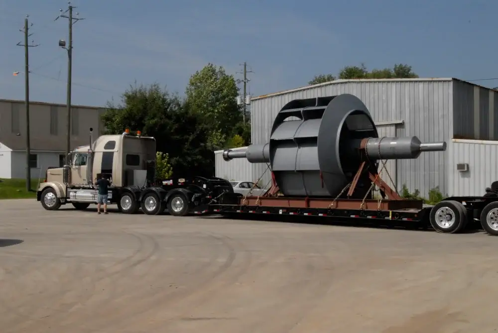 Truck transporting industrial fan on flatbed trailer.