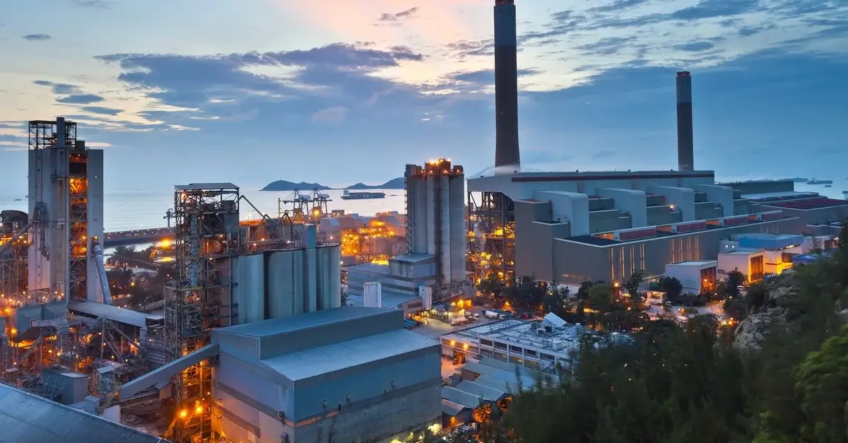 Industrial plant illuminated at dusk near the coastline.
