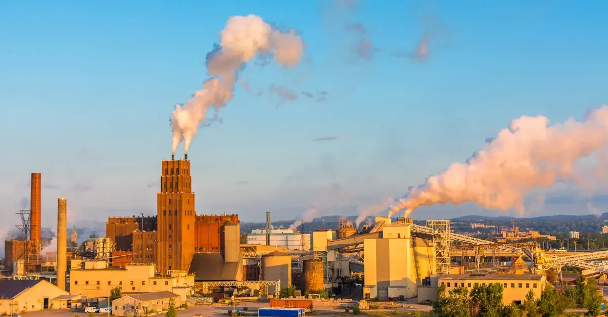 Factory emitting smoke against a clear blue sky.