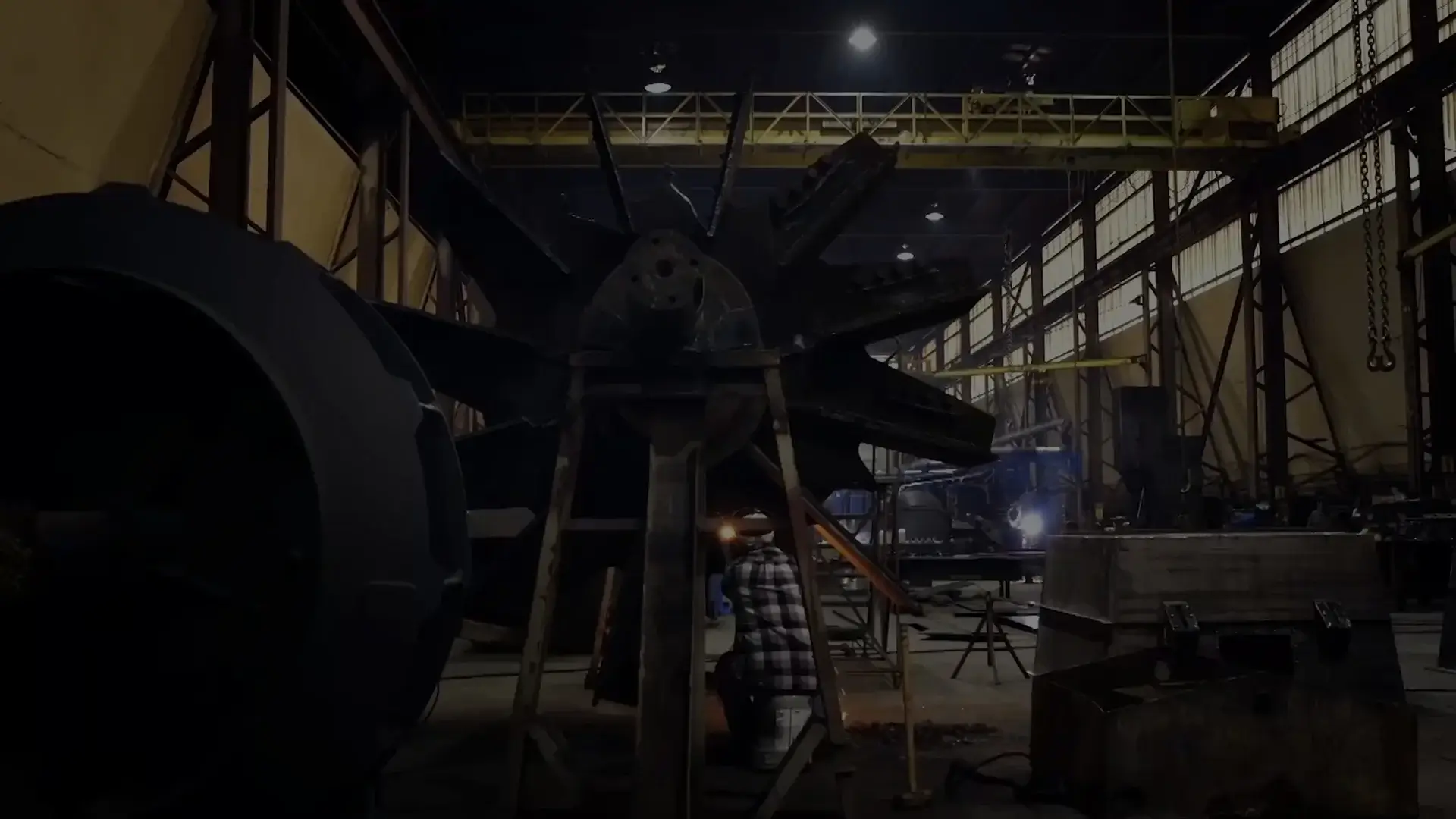 Welder fabricating a large industrial fan impeller inside a factory.