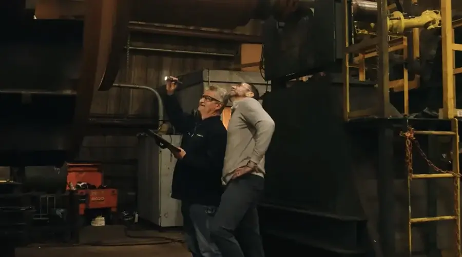 Two workers inspecting industrial equipment with flashlight.