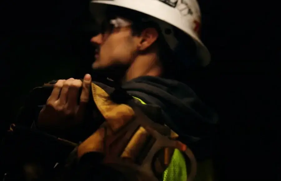 Worker carrying tools, wearing hard hat and safety gear.