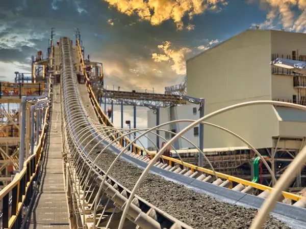Conveyor belt transporting material under cloudy sky.