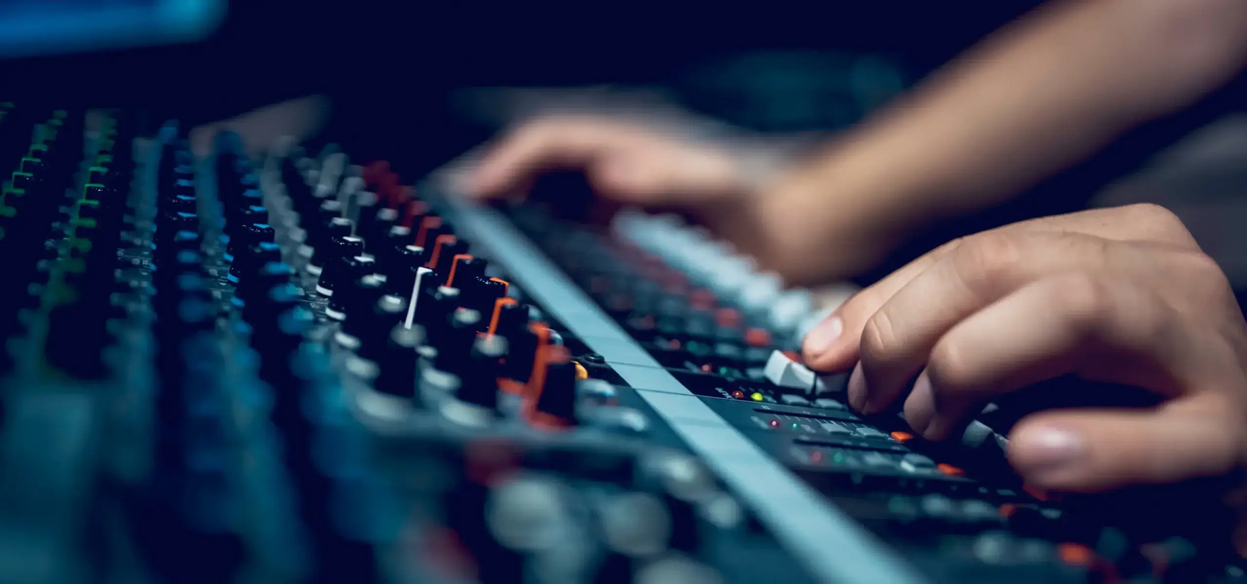 Hands adjusting audio mixing console controls.