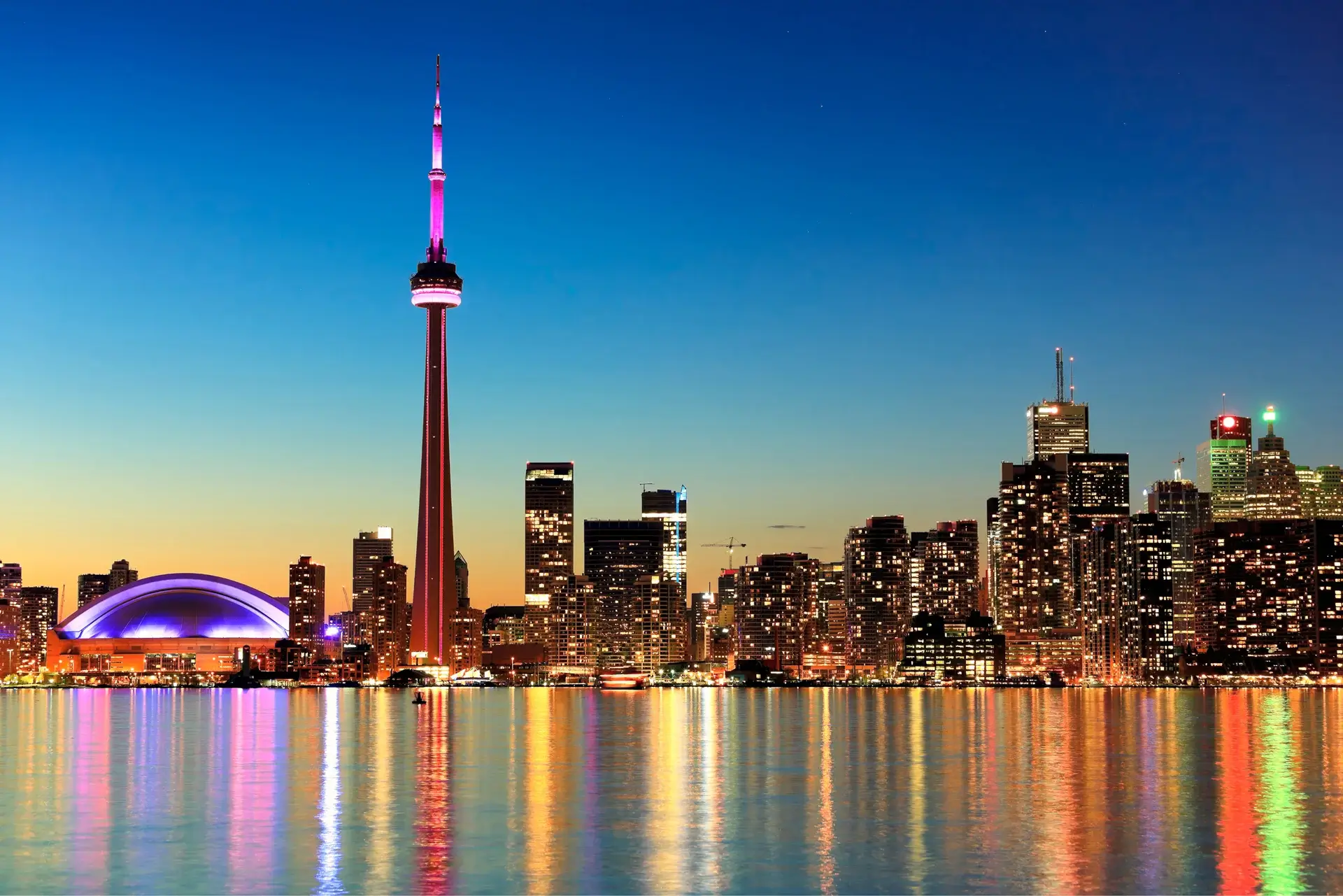 Skyline with illuminated tower reflected on water.