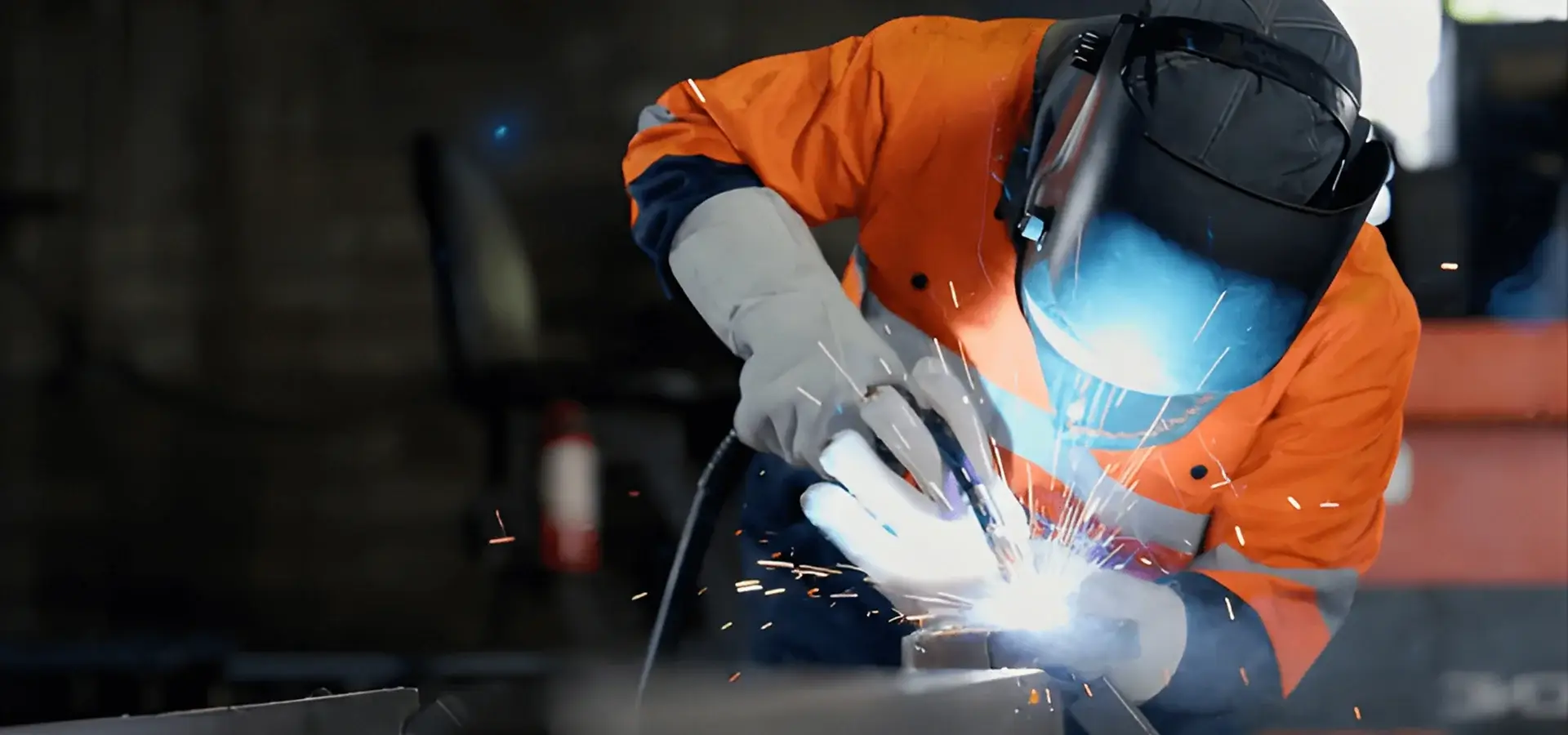 Welder in protective gear working with sparks flying.