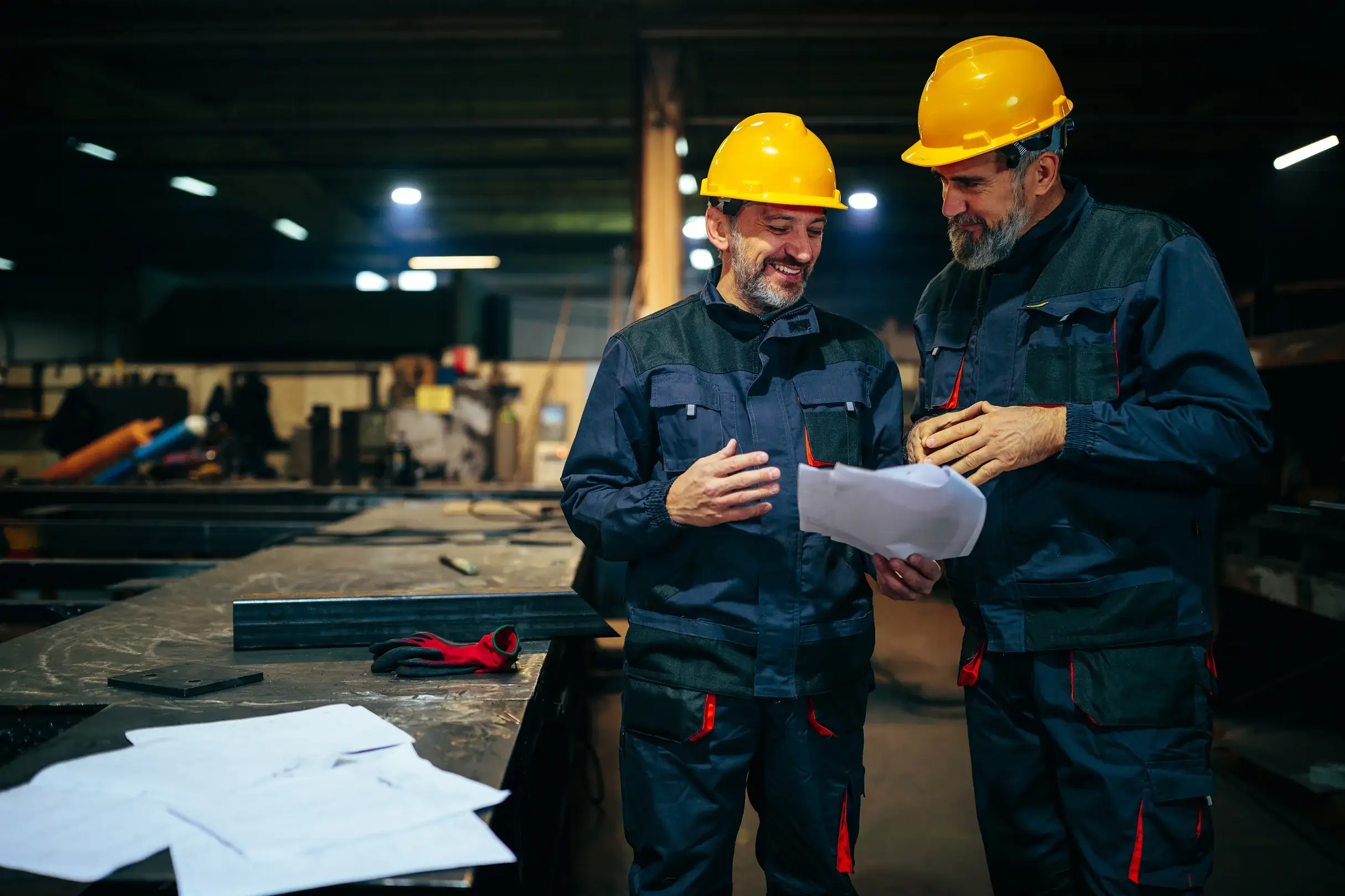 Two workers discussing plans in an industrial workshop.