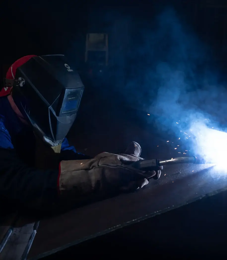 Welder using torch with protective gear, bright sparks flying.