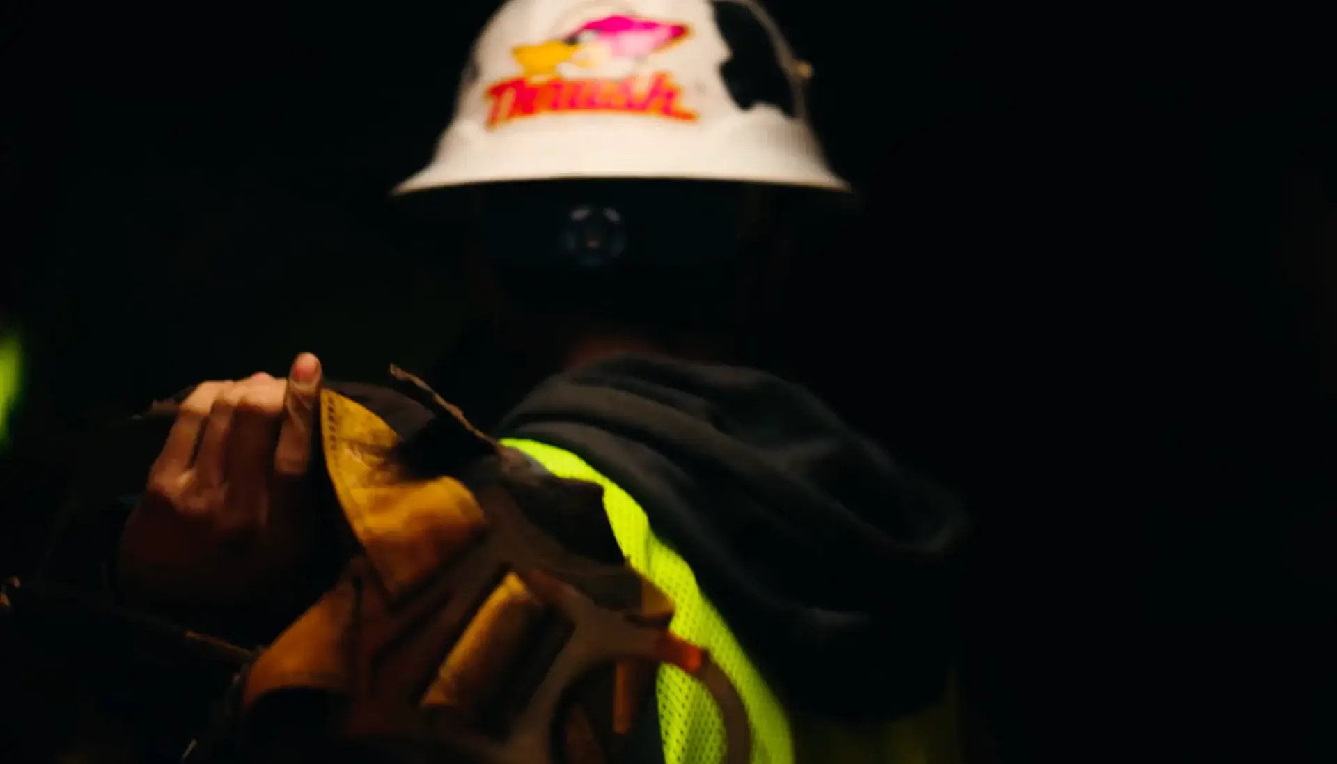 Worker holding tools, wearing hard hat and vest.