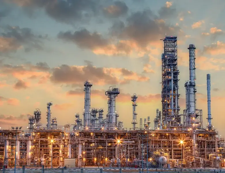 Industrial plant with towers under colorful sunset sky.