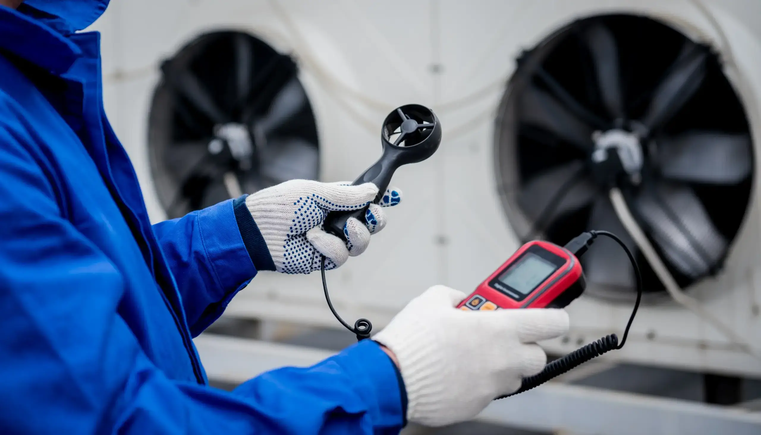 Technician measuring airflow near industrial fan.