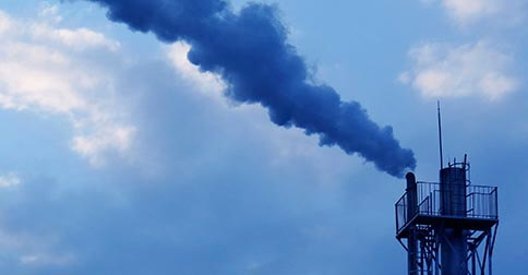 Industrial smokestack emitting dark smoke into sky.