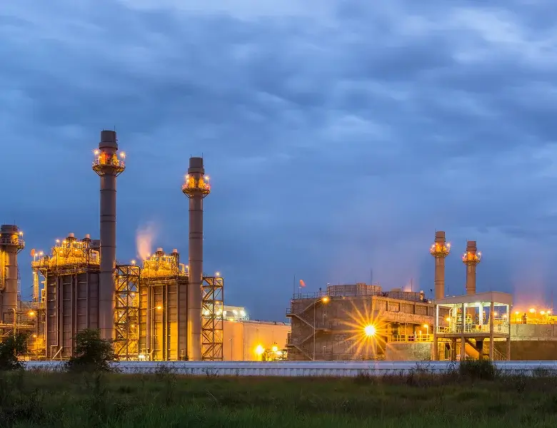 Industrial facility with tall chimneys illuminated at night.