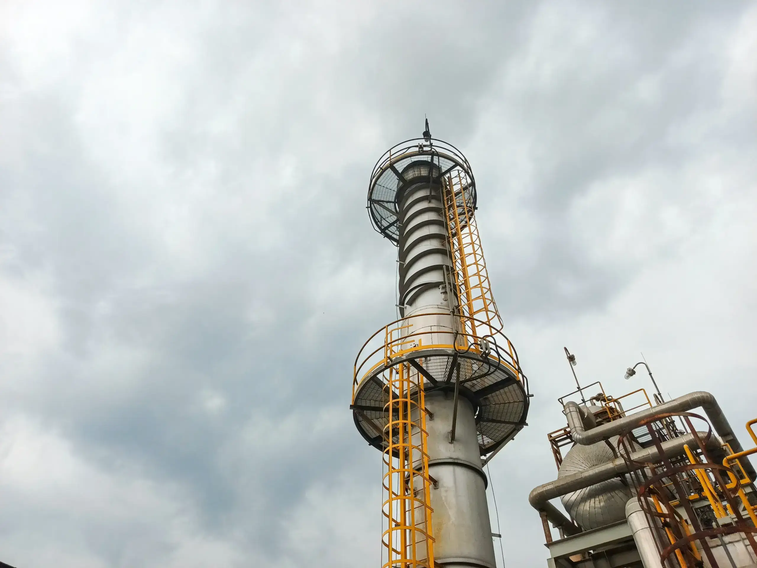 Industrial chimney with safety ladders under cloudy sky.