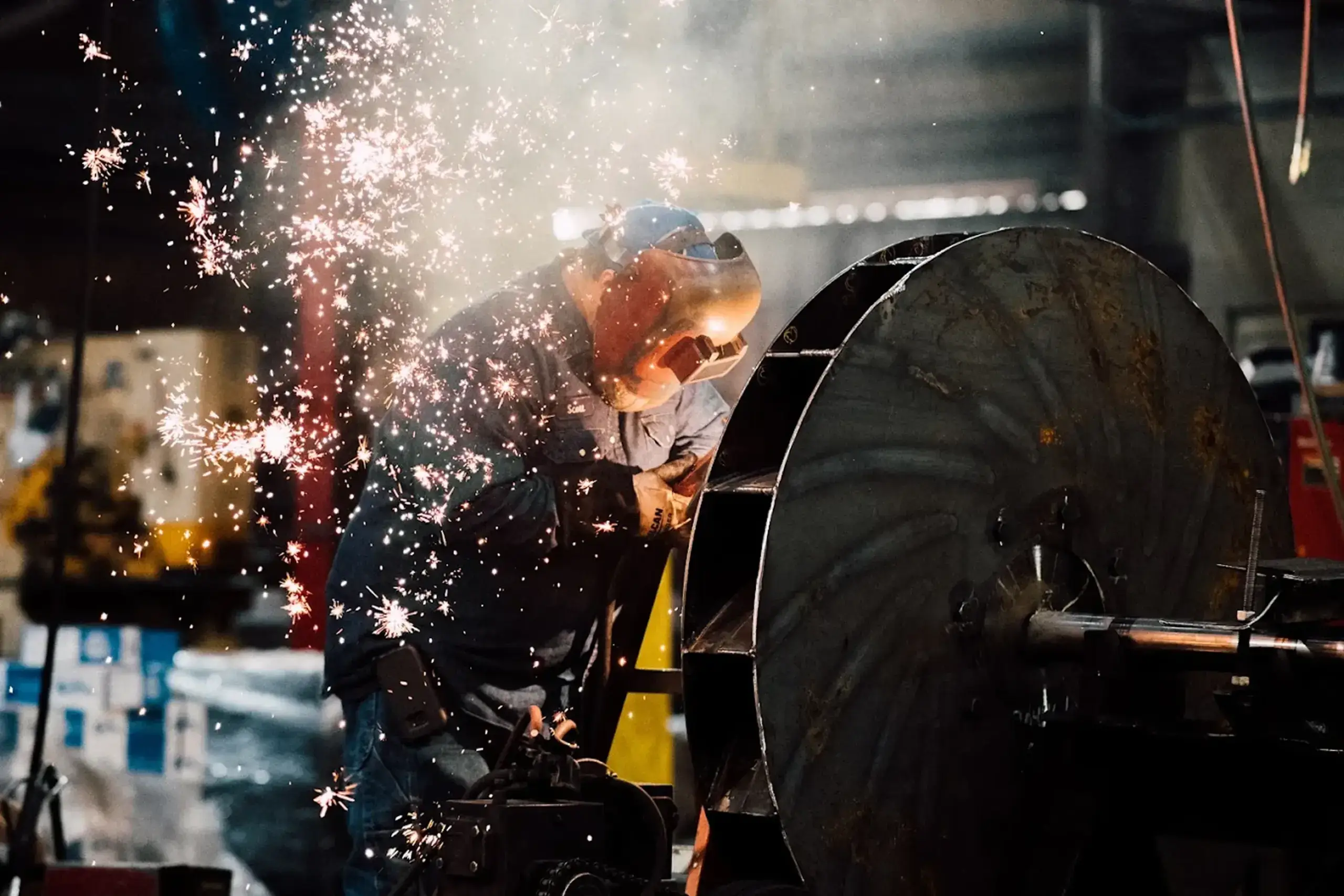 Welder crafting metal part, sparks flying around.