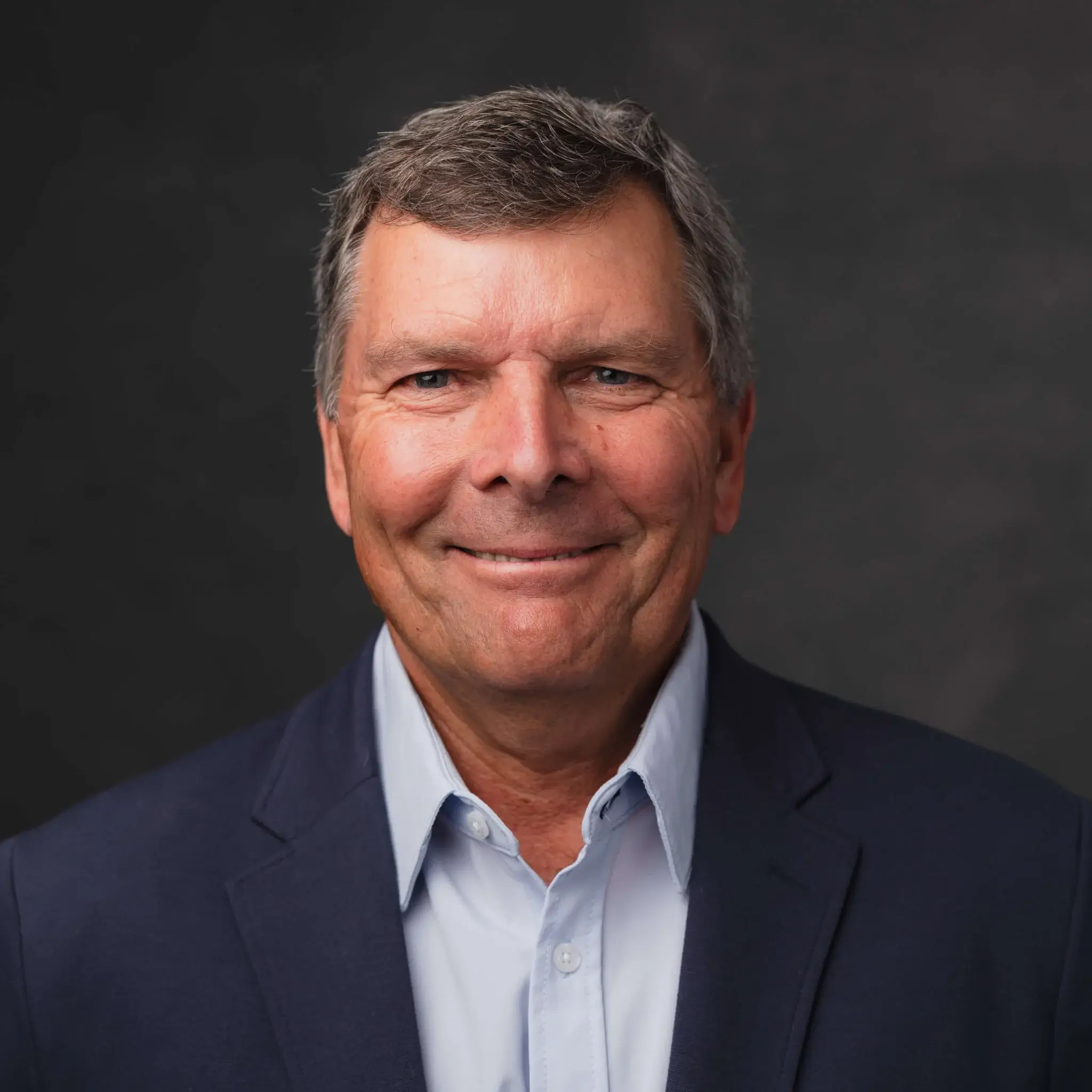 Smiling man in a suit against dark background.
