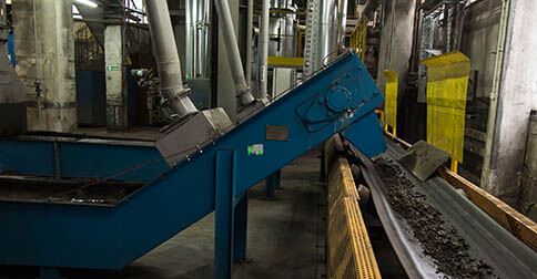Industrial conveyor belt transporting ash in a processing facility.