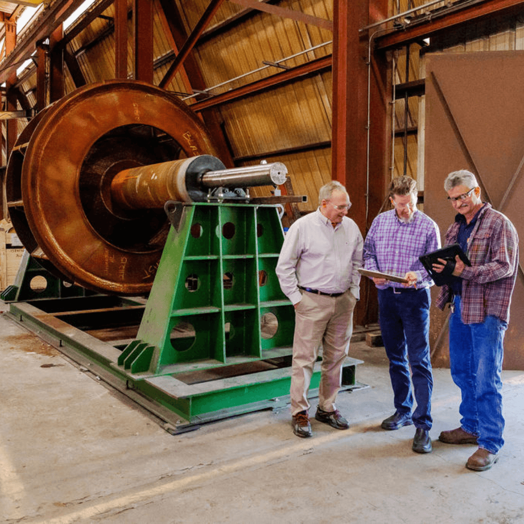 Engineers discussing plans beside large industrial fan component.