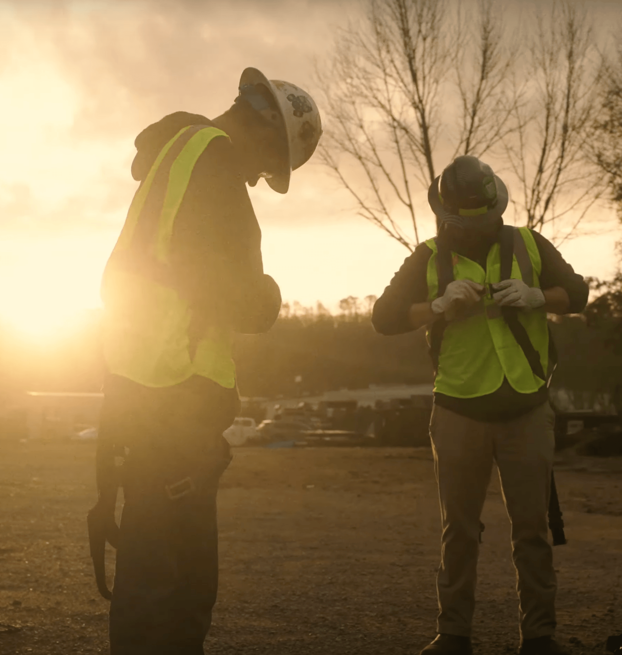 Workers adjusting safety gear at sunrise, wearing vests.