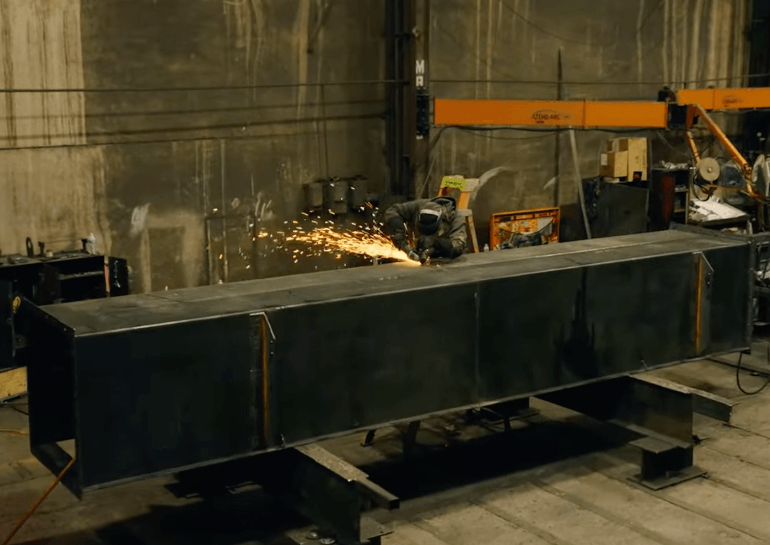 Worker welding large industrial component, sparks flying.