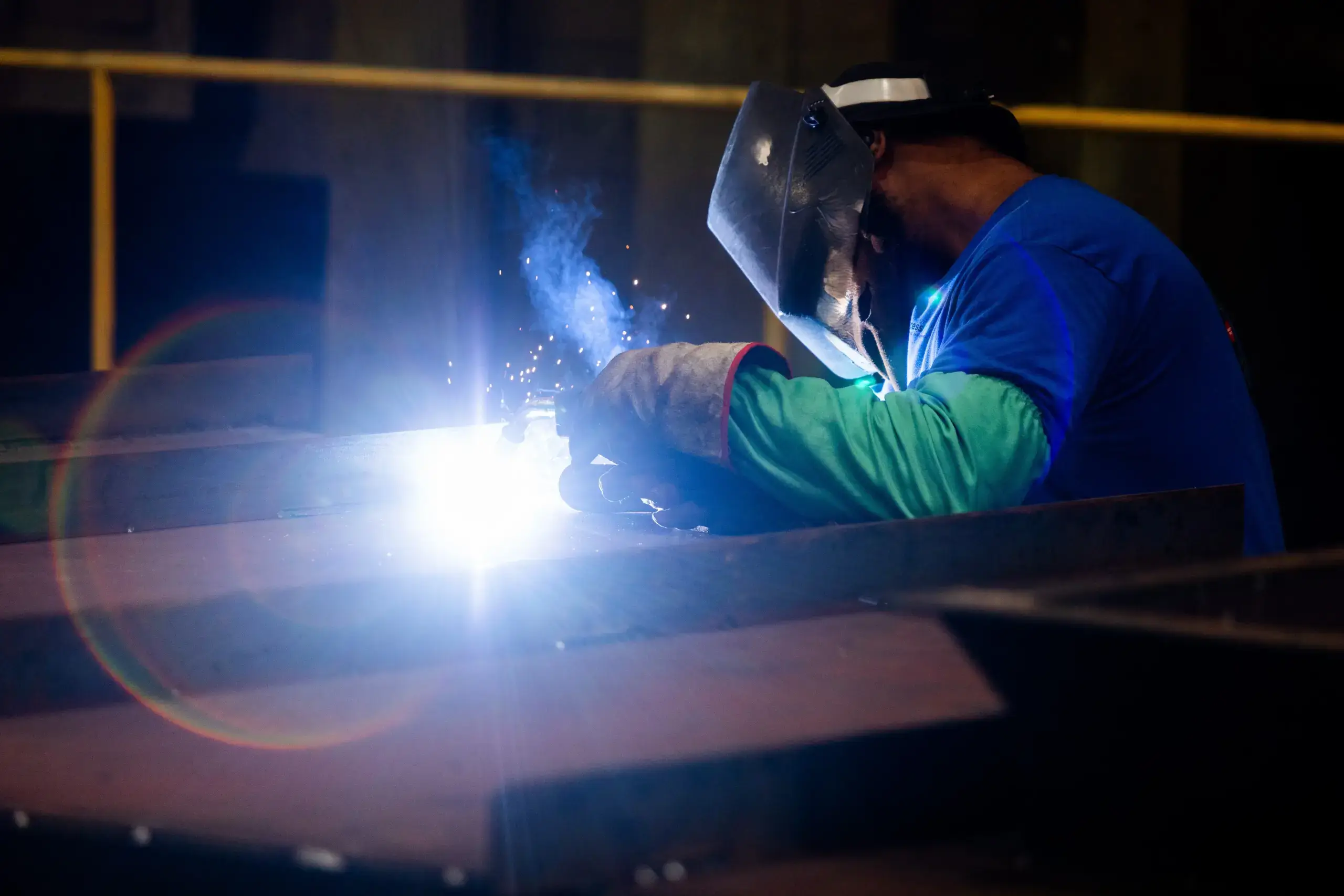 Welder in blue shirt working with bright sparks.
